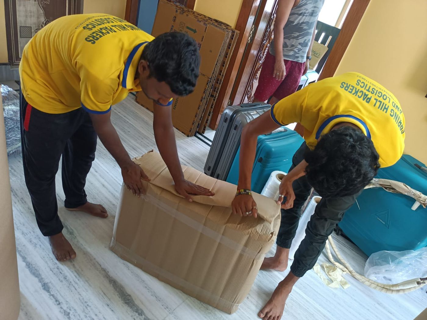 Two packers wrapping furniture on a tiled floor